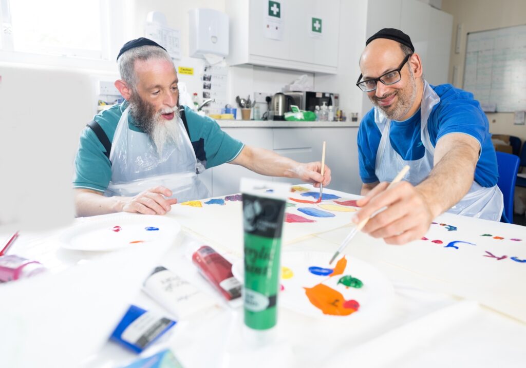 Two people wearing aprons holding paintbrushes while doing arts and crafts during an activity session